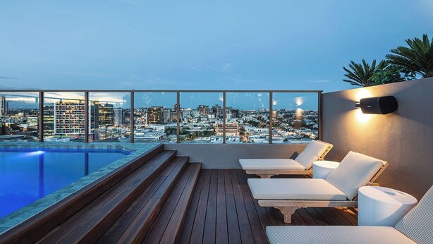 A rooftop pool area with lounge chairs, a wooden deck, and a city view.