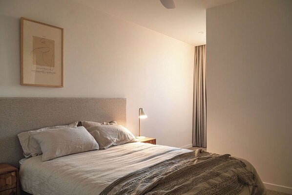 Une chambre à coucher avec un lit, une table de chevet, une lampe et un tableau encadré au mur.