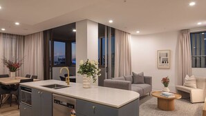 A modern apartment with a kitchen, dining area, and living room. It features a large window, a built-in dishwasher, and a coffee table. - Spacious & stylish apartment in James Street Precinct with pool, gym and rooftop (Fortitude Valley)