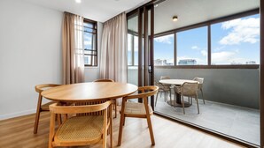 A modern dining area with a wooden table and chairs, large windows with curtains, and a view of the cityscape. - Spacious & stylish apartment in James Street Precinct with pool, gym and rooftop (Fortitude Valley)