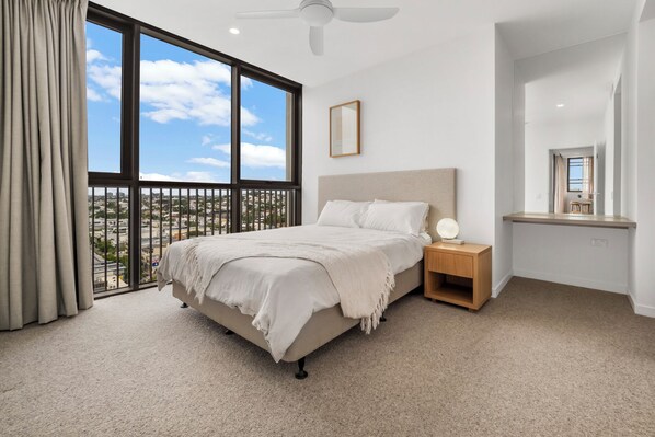 A bedroom with a bed, nightstand, and a view of the city through large windows.