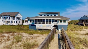 Una casa frente a la playa con una terraza de madera y una escalera que sube a un porche.