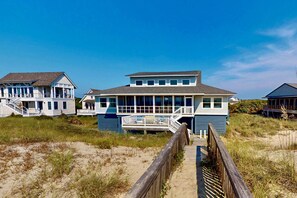 A beachfront house with a wooden deck and a staircase leading to a porch.