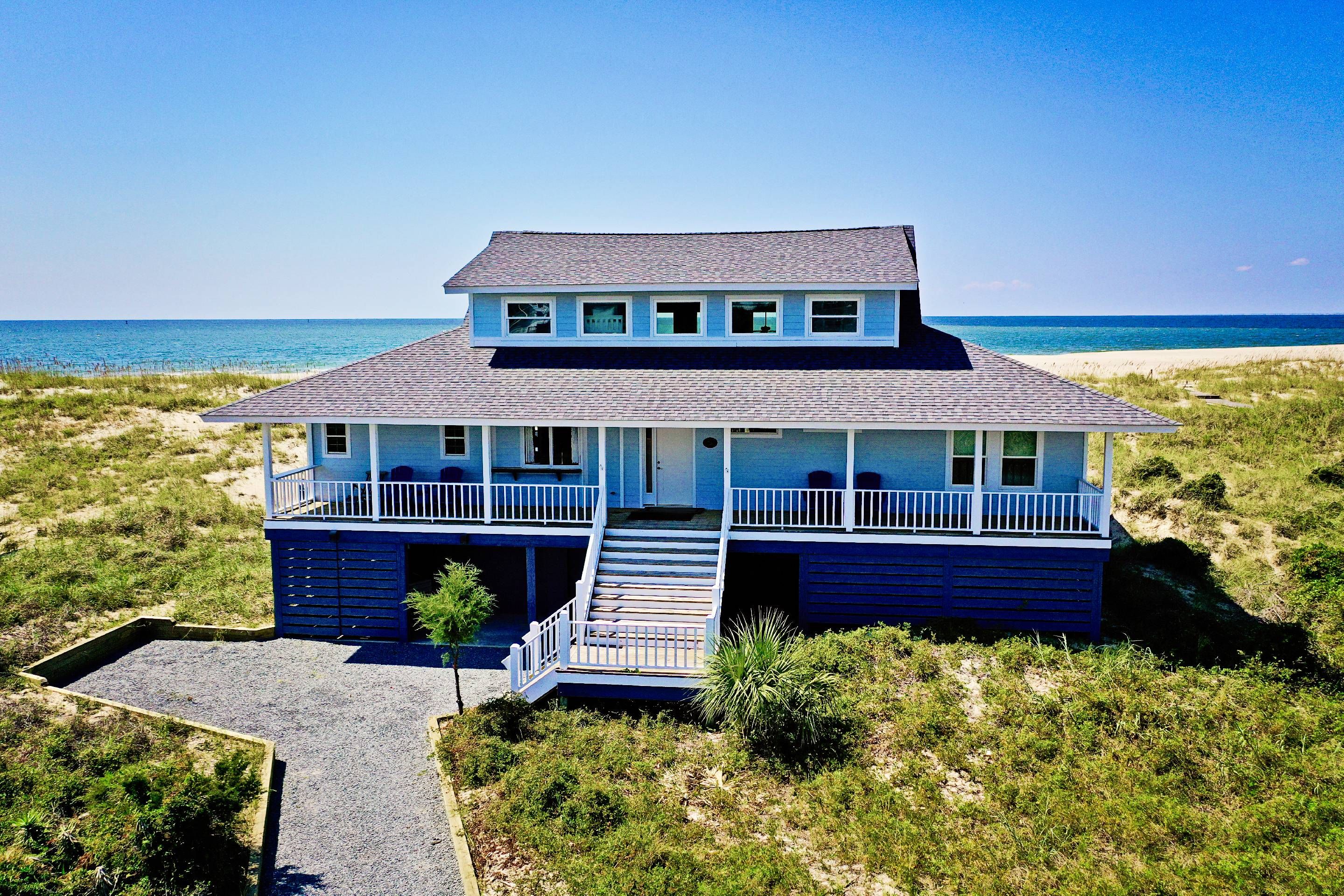 Ein zweistöckiges Strandhaus mit Balkon und überdachter Veranda.