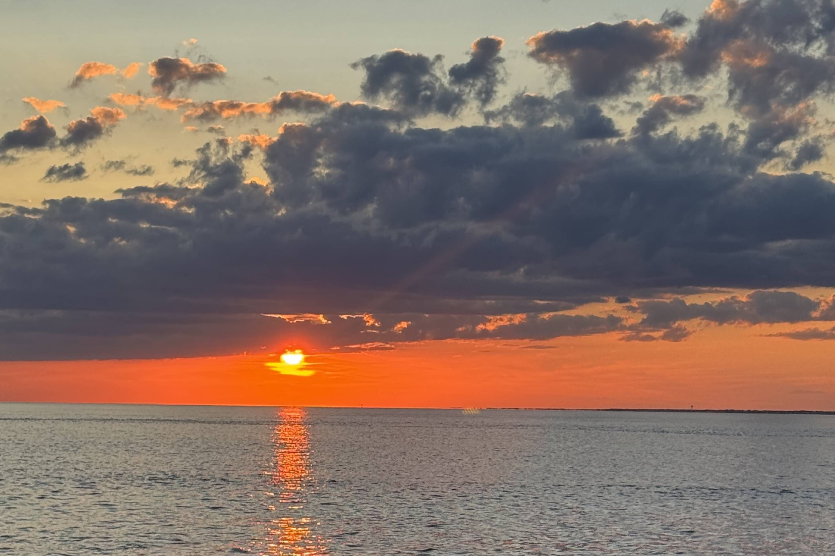 Una puesta de sol sobre un mar tranquilo con nubes en el cielo.