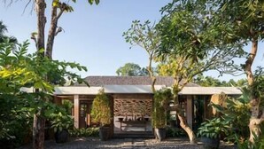 Un bâtiment moderne à la façade en pierre, entouré d’une végétation luxuriante et d’arbres.
