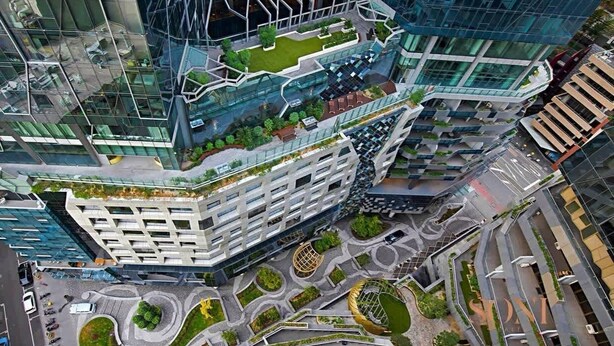 A modern high-rise building with a unique angular design, featuring multiple levels and a rooftop garden.