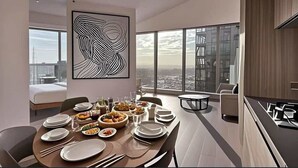 A modern dining area with a large table set for a meal, a city view through large windows, and a contemporary art piece on the wall.