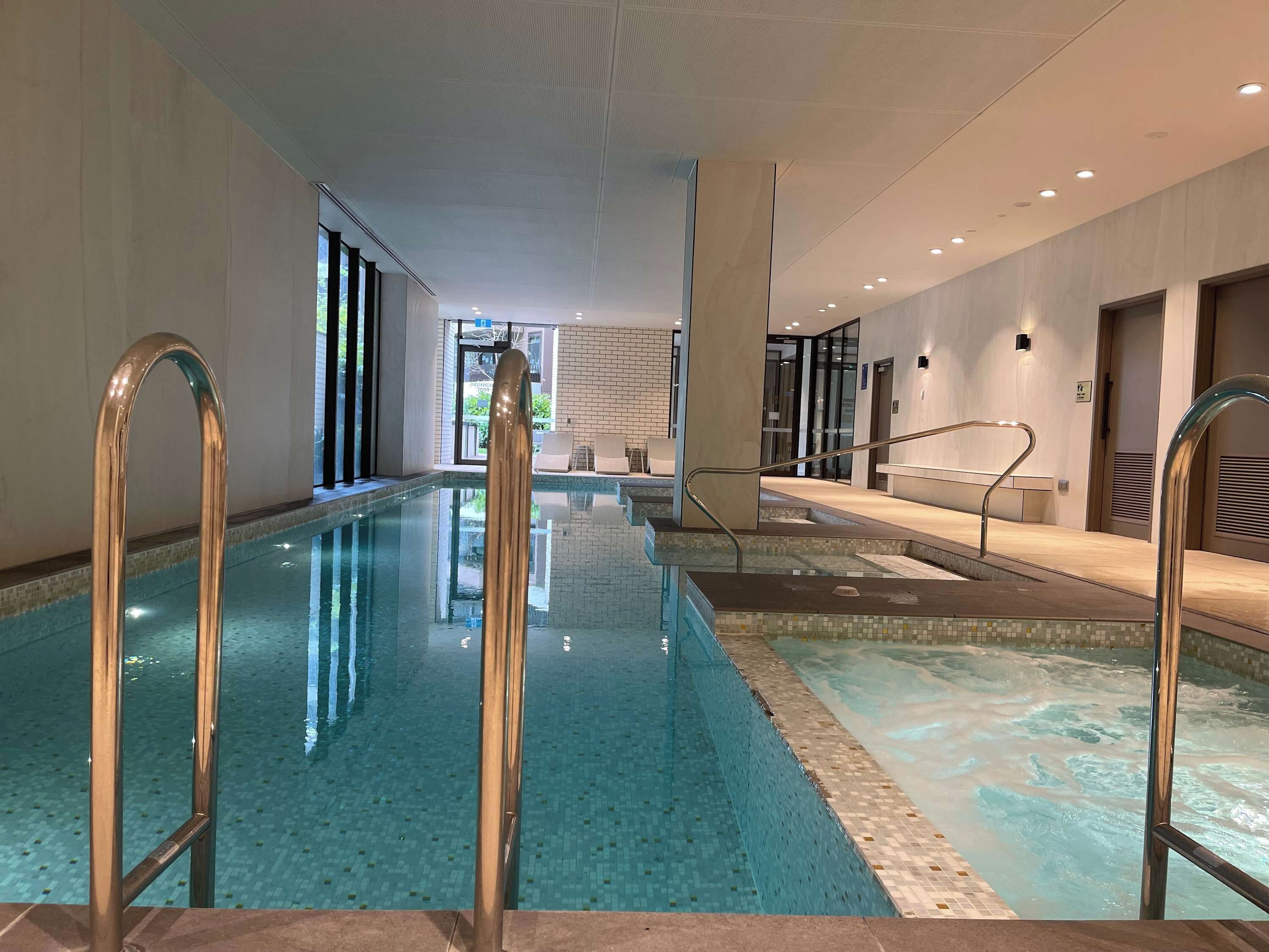 An indoor swimming pool with clear water, metal handrails, and a tiled floor.