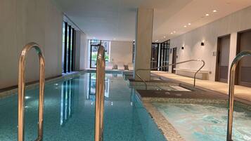 An indoor swimming pool with clear water, metal handrails, and a tiled floor.