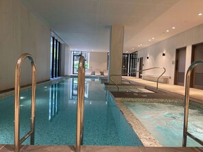 Une piscine intérieure à l’eau claire, dotée de rampes métalliques et d’un sol carrelé.