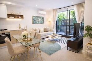 A modern living room with a glass dining table, sofa, and TV stand.