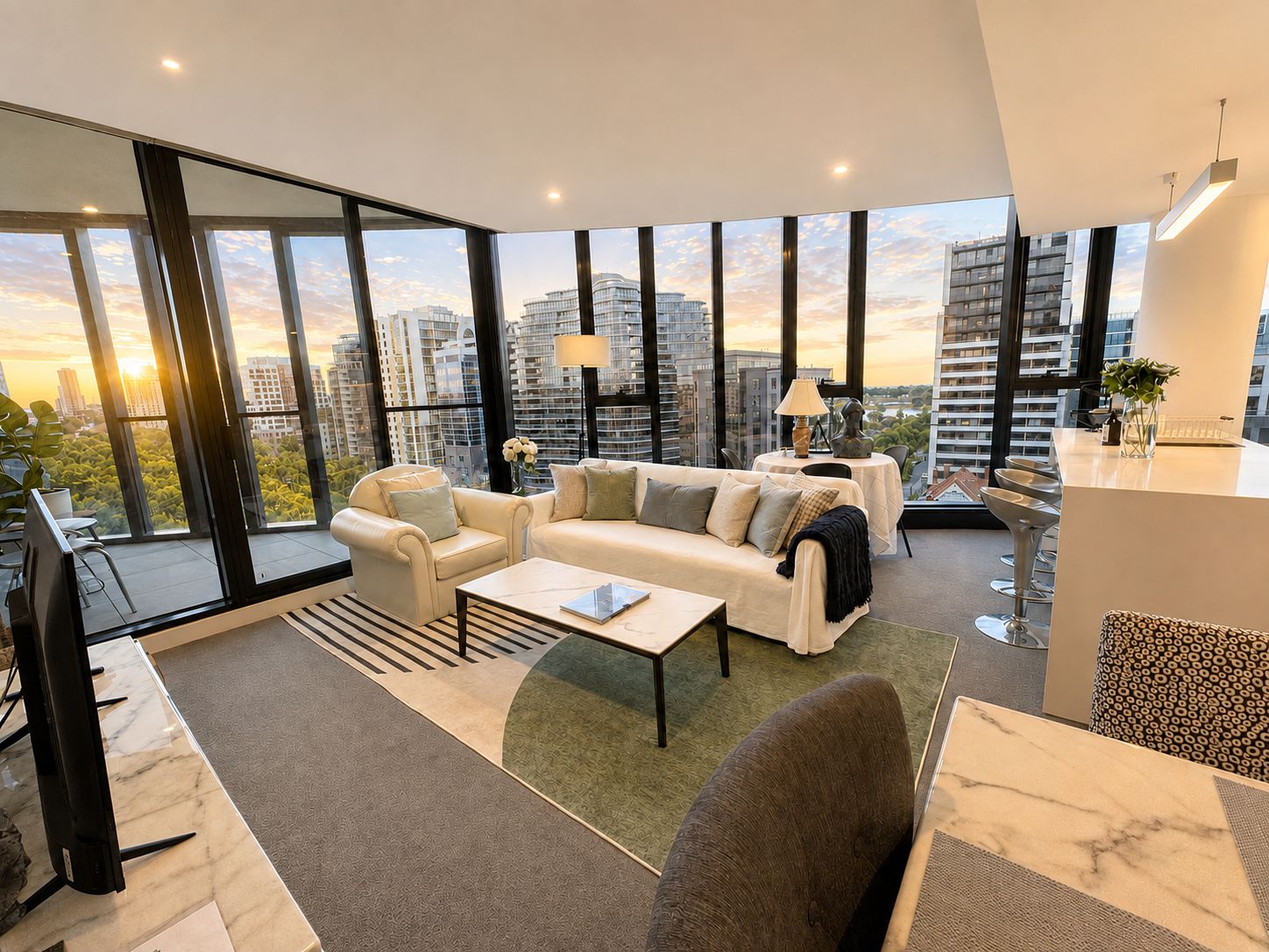 A modern living room with a sofa, armchairs, a coffee table, and a dining area with a marble table. Large windows offer a view of the cityscape.