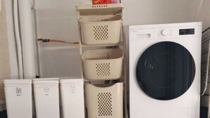 Un espace buanderie comprenant un lave-linge, des paniers à linge empilés et une poubelle.