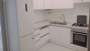 Une cuisine de taille réduite avec des meubles blancs, un four encastré, un évier et une cuisinière.