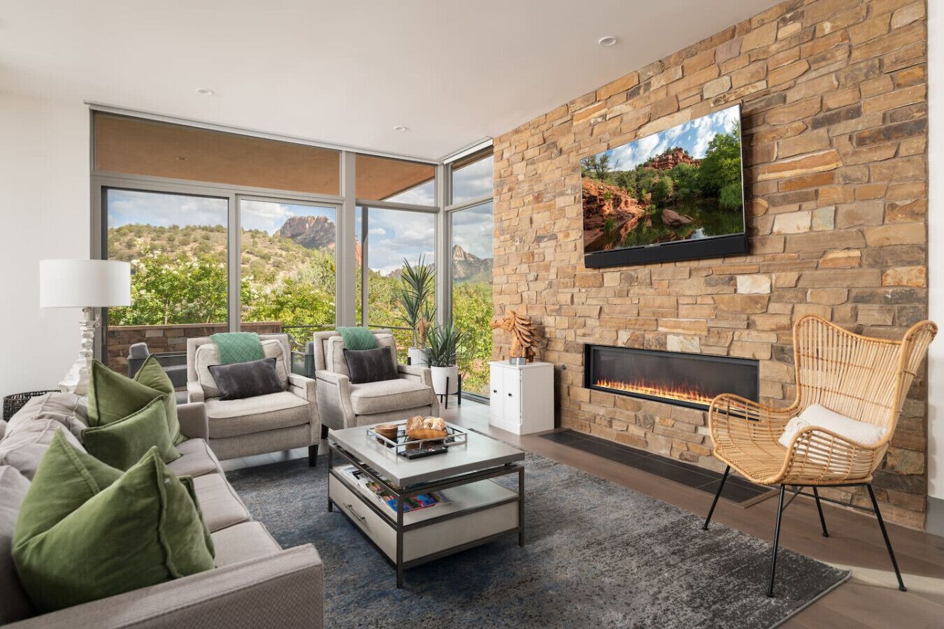 A modern living room with a stone wall, a fireplace, comfortable seating, and large windows offering a view of the outdoors.
