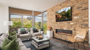 A modern living room with a stone wall, a fireplace, comfortable seating, and large windows offering a view of the outdoors. - Luxury Townhome - Exclusive guest access to a members-only golf club and resort amenities including pool. (Sedona)