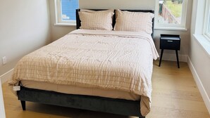 Une chambre à coucher avec un lit, deux fenêtres, une table de chevet et un luminaire au plafond.