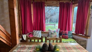 Ein gemütliches Blockhaus-Interieur mit einem Holzesstisch, roten Vorhängen und einer Bank mit Kissen.