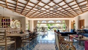 A spacious room with a high ceiling and a patterned floor, featuring a dining area with chairs and tables, a sofa, and a view through large windows. - Sayang d'Amour by Elite Havens (Seminyak)