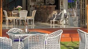 An outdoor seating area with wicker furniture and a glass table, overlooking a street with buildings and a blue sky. - Sayang d'Amour by Elite Havens (Seminyak)