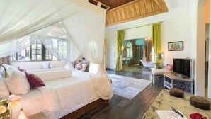 A bedroom with a canopy bed, a sitting area with a sofa, a television, and a desk. - Sayang d'Amour by Elite Havens (Seminyak)