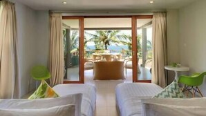 A hotel room with two beds, a balcony with a table and chairs, and a view of palm trees and the sea.