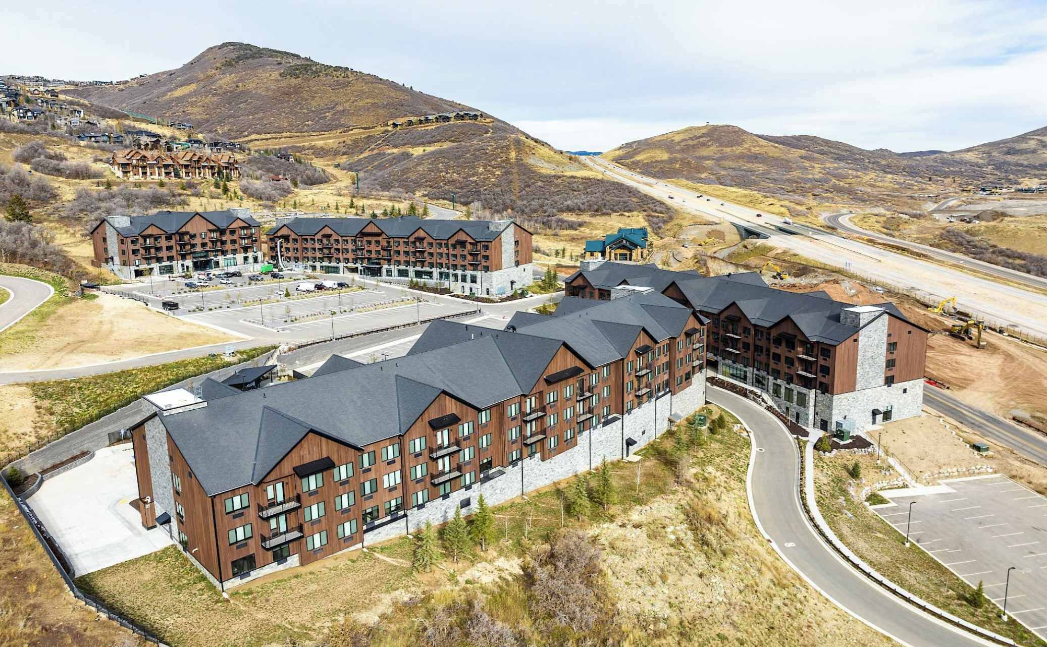 A modern hotel with multiple buildings, a parking lot, and a mountainous backdrop.