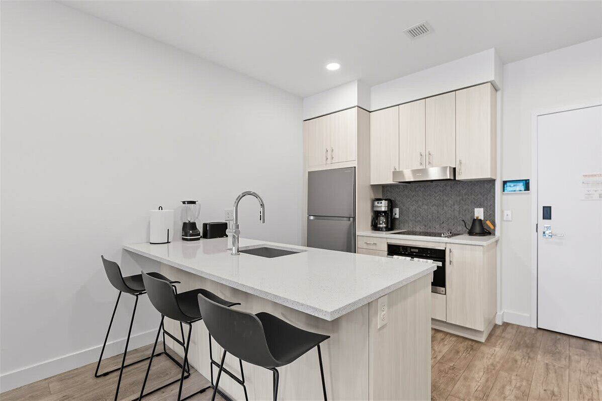 A modern kitchen with a central island, bar stools, a built-in oven, and a refrigerator.