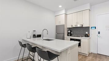 A modern kitchen with a central island, bar stools, a built-in oven, and a refrigerator.