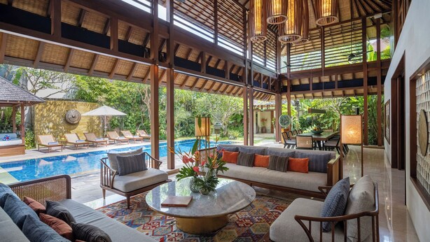 A spacious outdoor lounge area with a pool, comfortable seating, and a view of lush greenery. - Villa Windu Sari by Elite Havens (Seminyak)