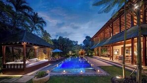 A pool area with a water feature, surrounded by a well-maintained lawn and a building with large windows. - Villa Windu Sari by Elite Havens (Seminyak)