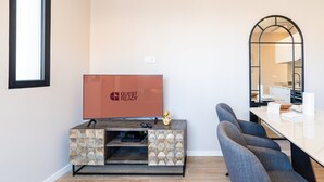 Una habitación de hotel moderna con televisor de pantalla plana, una mesita de noche con diseño de piedra, una zona de estar con espejo y vistas a la cocina.