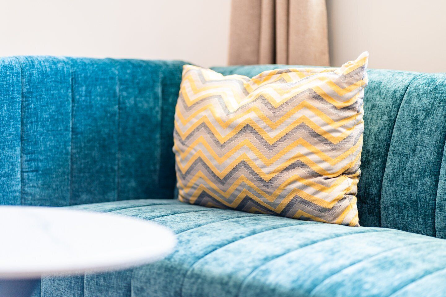 A teal sofa with a chevron-patterned pillow.