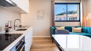 Una cocina compacta con estufa moderna, lavamanos y zona de comedor con mesa y sofá azul.