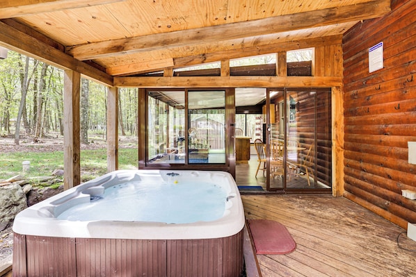 Una cabaña de madera con jacuzzi, puertas de vidrio que dan a una terraza y vistas al bosque.