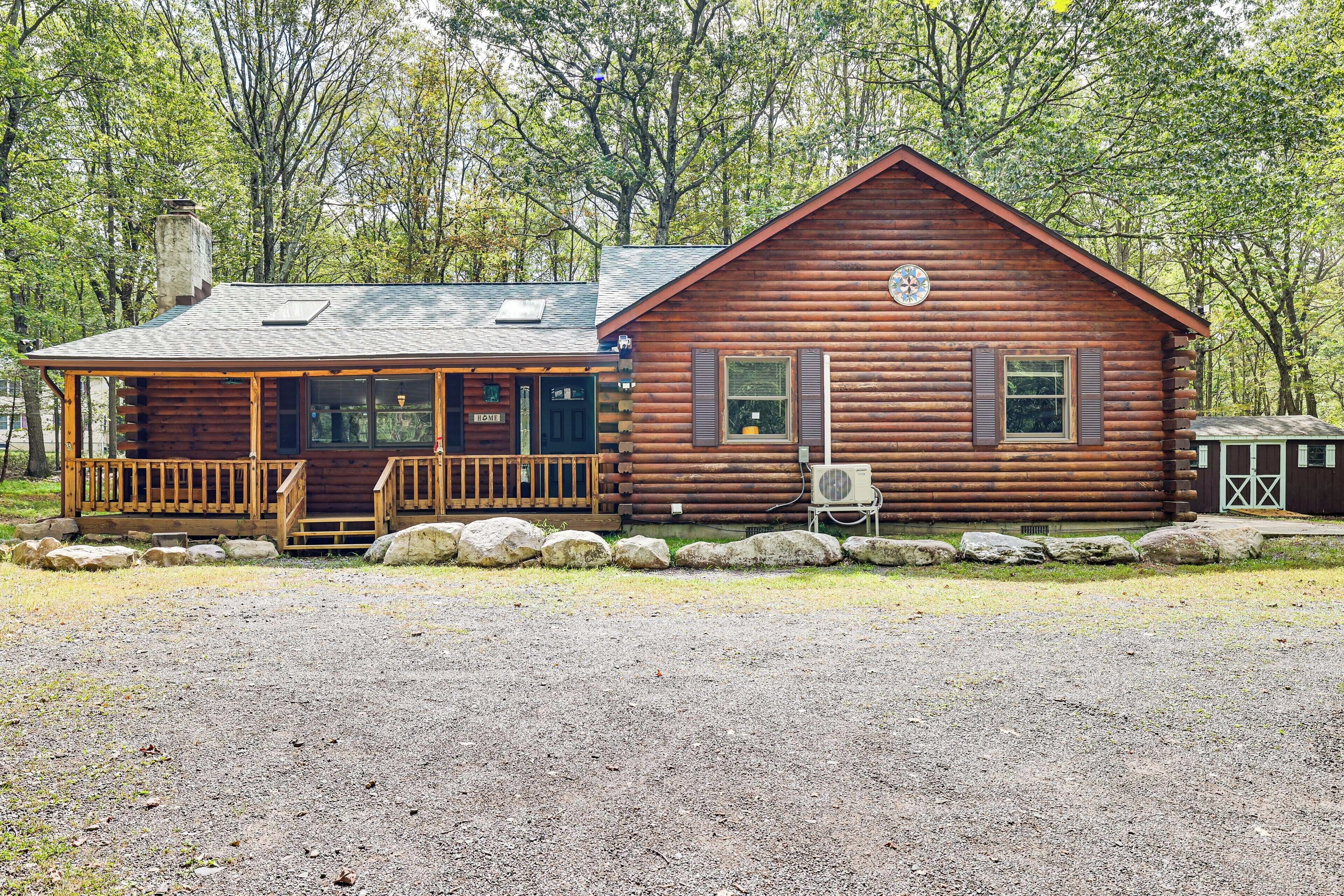 A rustic log cabin with a porch and a small attached building, surrounded by trees.