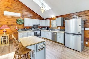 Una cocina con paredes de madera, una isla central, electrodomésticos de acero inoxidable y una lámpara colgante.