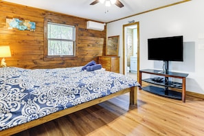 Un dormitorio con una cama de madera, un televisor sobre un mueble bajo y una ventana con persianas.