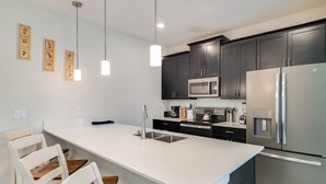 A modern kitchen with dark cabinets, stainless steel appliances, a white countertop, and pendant lighting. - Pet Friendly! Townhome w/ Pool in ChampionsGate (Kissimmee)