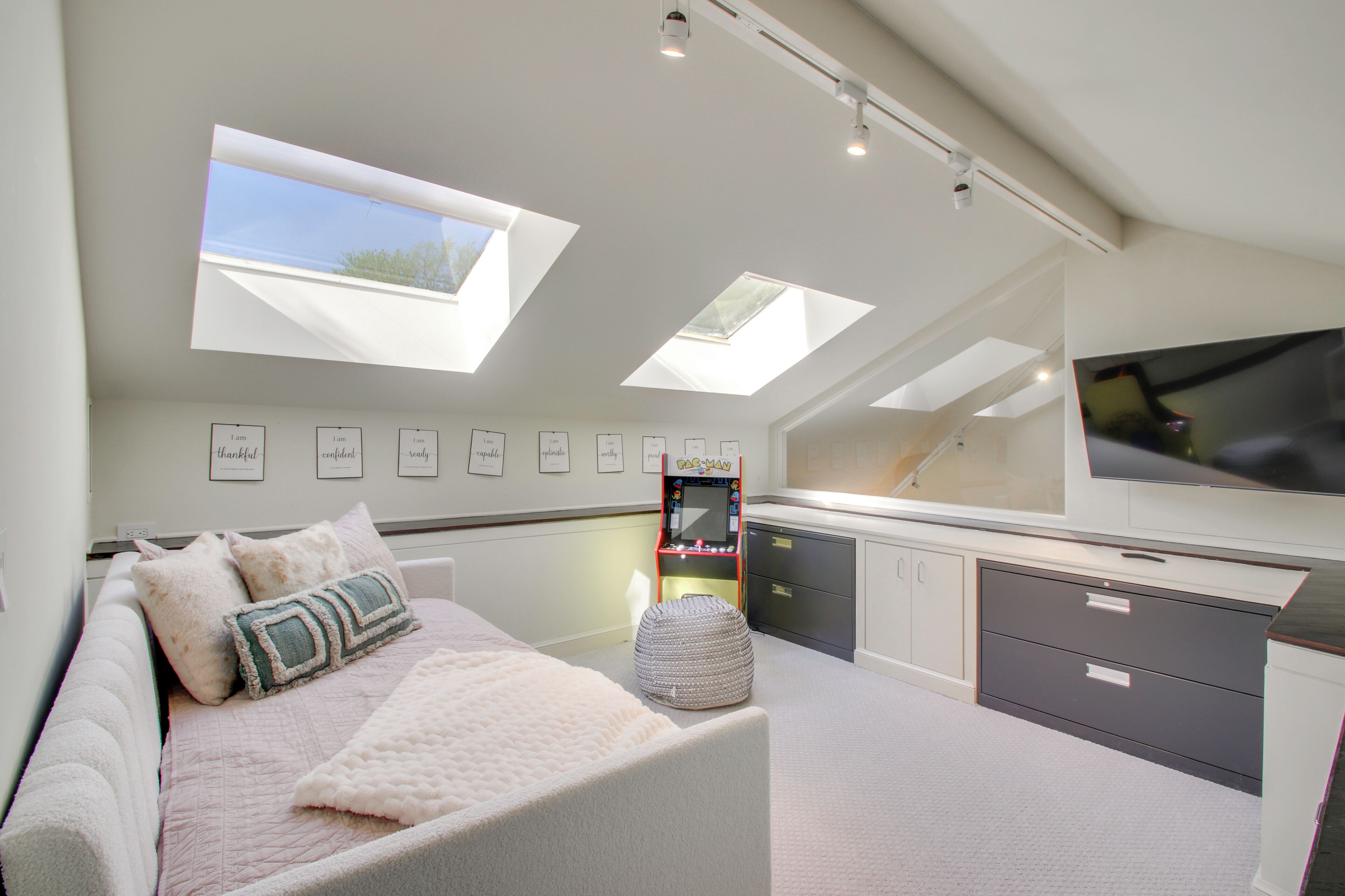 A bedroom with a bed, a TV, a desk, and skylights.