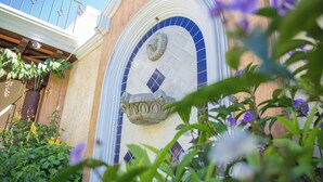 Fachada de edificio con un arcoado de azulejos azules, barandilla de piedra y una maceta colgante.