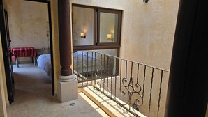 Un pasillo de hotel con una cama, una mesa con mantel a rayas y un ventanal con vista al balcón.