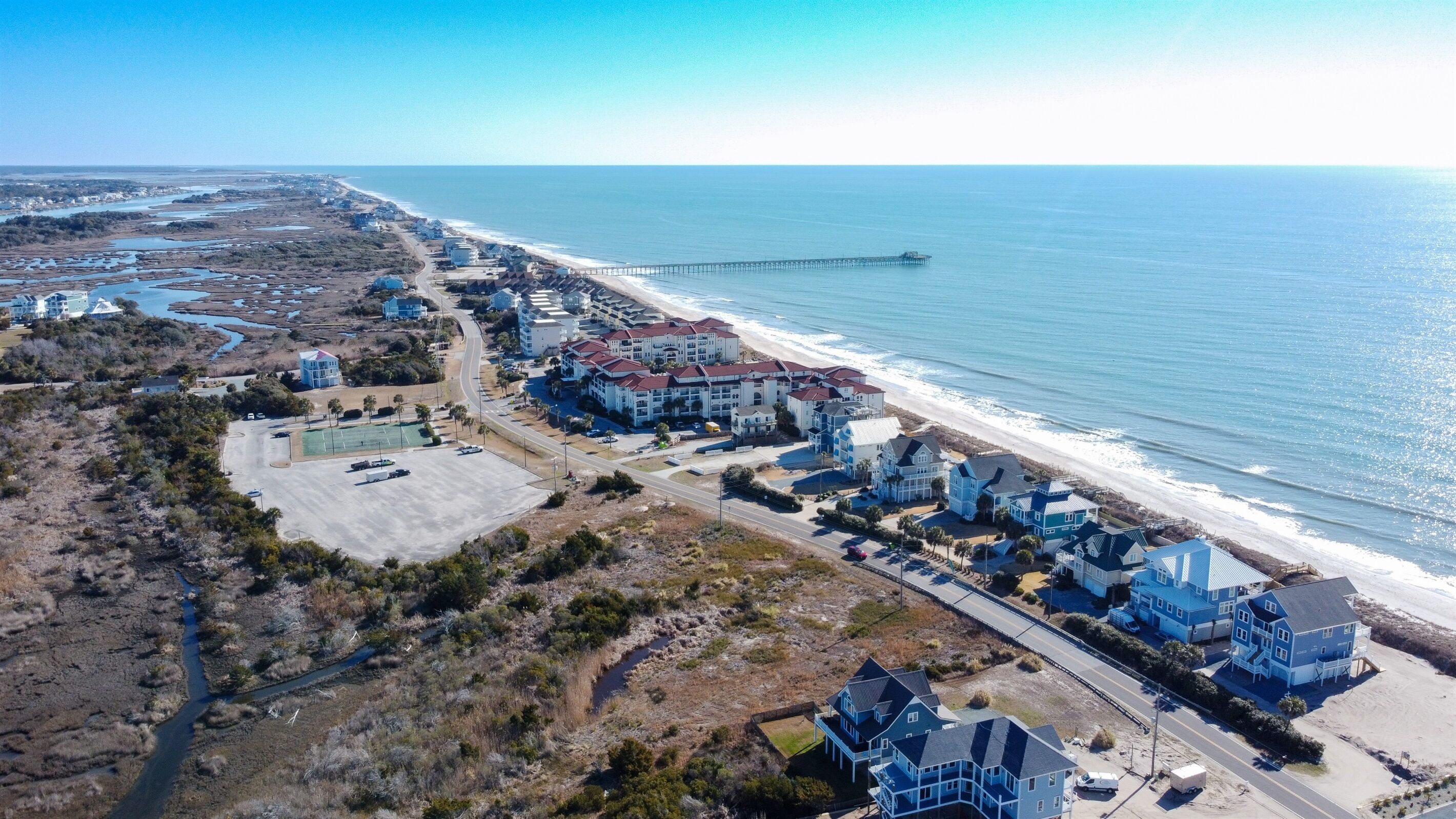 An aerial view of a coastal residential area with beachfront properties, a pier, and a road leading to the beach.