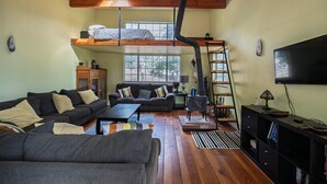 A cozy living room with a sofa, coffee table, and a TV. There is a loft bed above and a ladder leading to it.