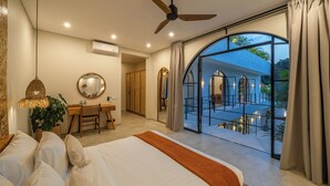 Camera da letto con un grande letto, una scrivania, una sedia, un ventilatore a soffitto e vista su un balcone esterno.