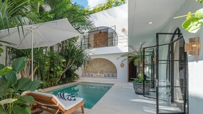 Ein moderner Poolbereich im Innenbereich mit Liegestuhl, weißem Sonnenschirm und üppiger tropischer Bepflanzung.