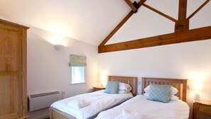 A bedroom with two beds, wooden beams, a wardrobe, a radiator, and a window with a curtain.