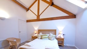 A bedroom with a wooden ceiling, a bed with pillows, a nightstand, a chair, and a door.
