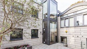 A modern building with a glass elevator shaft, numbered units 3 to 5, and a small garden area with flowers. - Tufnell Park retreat close to Hampstead Heath (London)
